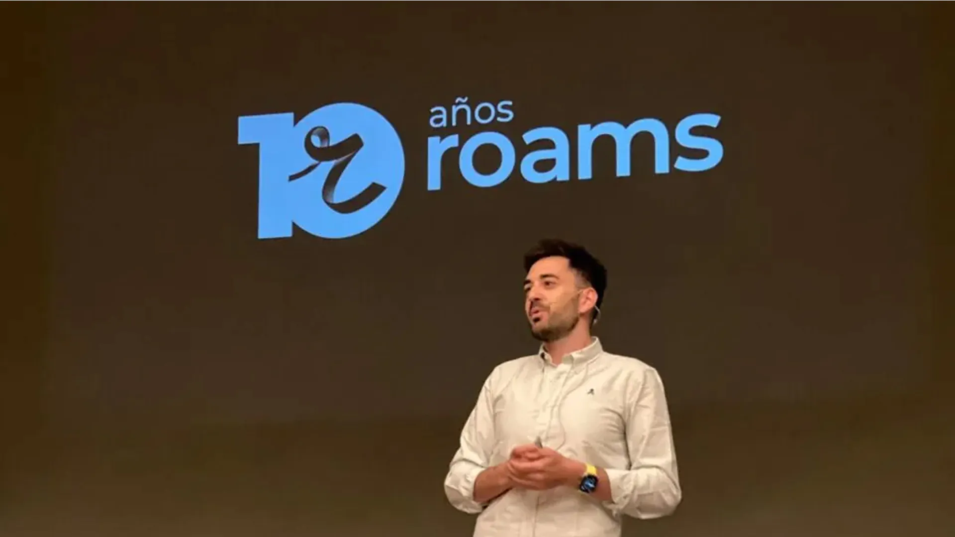 Eduardo Delgado da una charla en un escenario frente a una pantalla con el logo del 10.º aniversario de Roams.