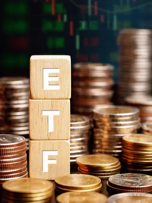 Bloques de madera con siglas ETF rodeados de monedas para representar la inversión en fondos cotizados en bolsa.