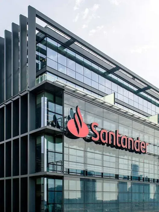 Fachada de un edificio corporativo del Banco Santander, con su gran logotipo rojo visible en la pared acristalada de la oficina.