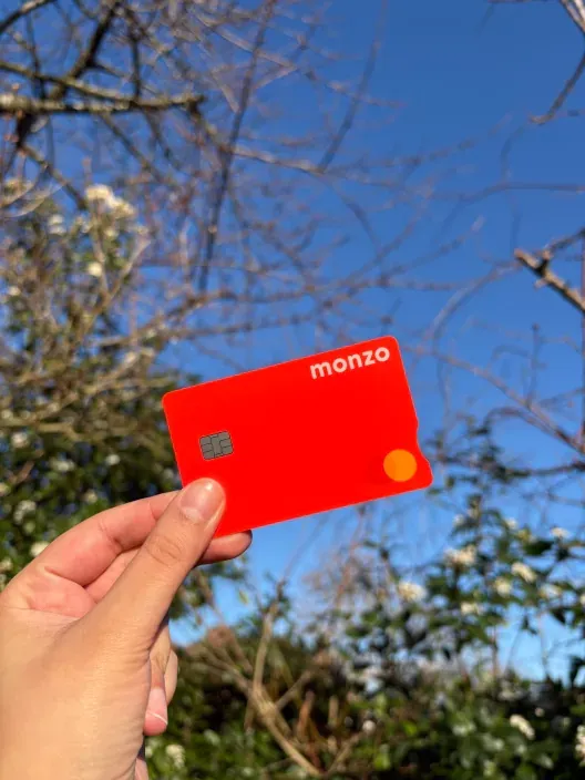Mano sosteniendo una tarjeta roja de Monzo al aire libre