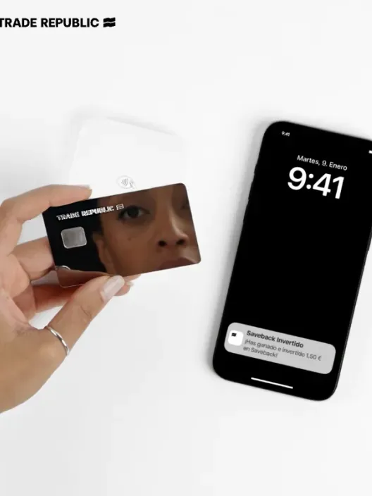 Mano sosteniendo la tarjeta de débito de Trade Republic. Un móvil al lado muestra una notificación del Saveback de 1,50€ ganado.