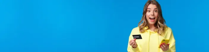 Mujer joven sorprendida con tarjeta de crédito y móvil para compras online o pagos digitales.