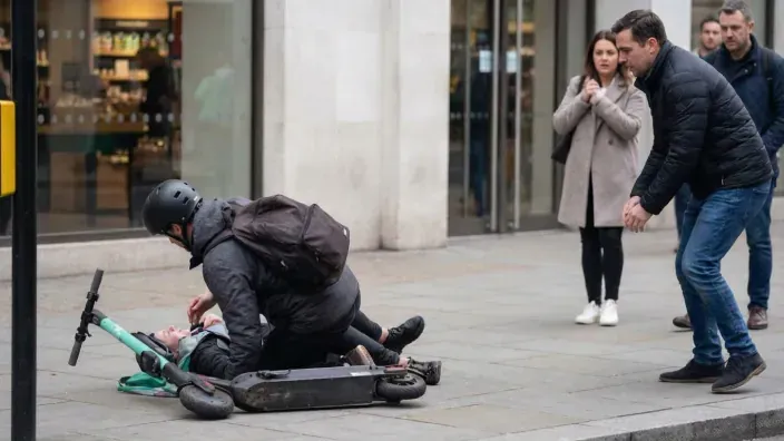 Peatones ayudando a usuario caído tras accidente con patinete eléctrico en vía pública.
