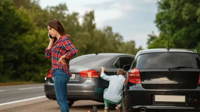 Mujer llamando por teléfono después de un accidente de tráfico entre dos coches en la carretera