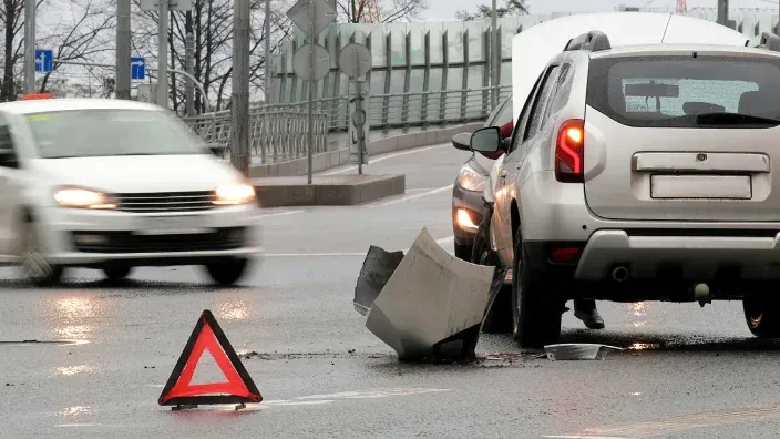 Accidente de tráfico con coche detenido y triángulo de emergencia en carretera mojada.