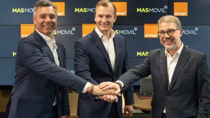 Tres directivos estrechando las manos frente a pantallas con los logotipos de Orange y MásMóvil.