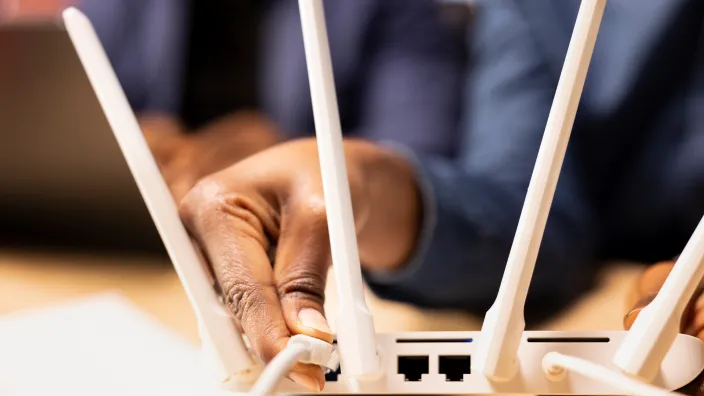 Una persona conecta un cable a un router blanco con antenas, configurando la red de internet en casa.