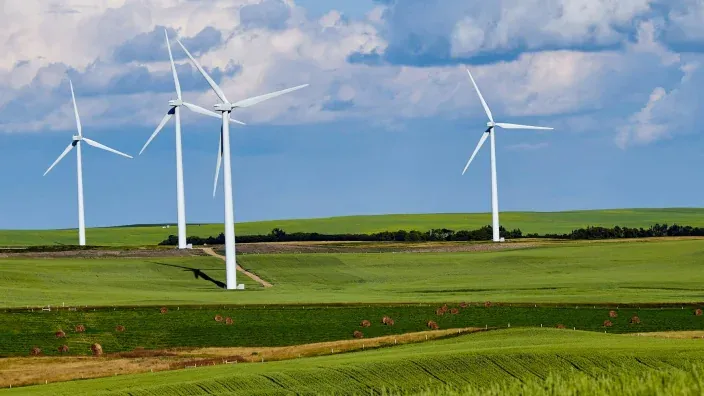 Aerogeneradores de un parque eólico situados en un campo verde bajo cielo parcialmente nublado.