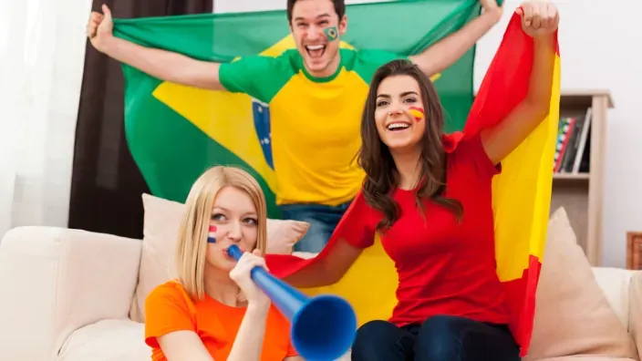 Aficionados celebrando el Mundial de fútbol con banderas y vuvuzela en casa para ver deporte en streaming.