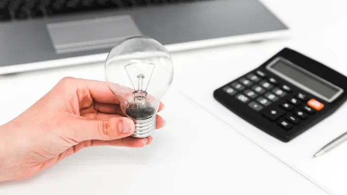 Mano sosteniendo una bombilla junto a una calculadora para representar el ahorro energético y el coste de la factura de la luz.