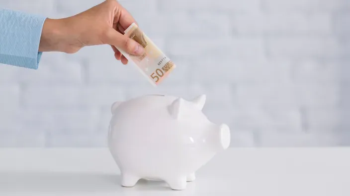 Mano metiendo un billete de 50 euros en una hucha.