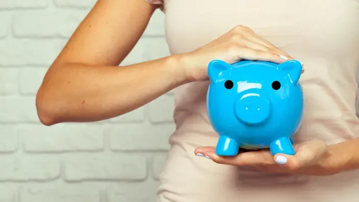 Mujer con hucha de cerdito azul para representar el ahorro y la inversión financiera personal.