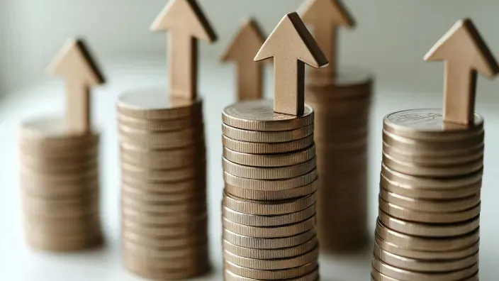 Pilas de monedas con flechas hacia arriba que simbolizan el aumento de la rentabilidad del ahorro y los depósitos bancarios.