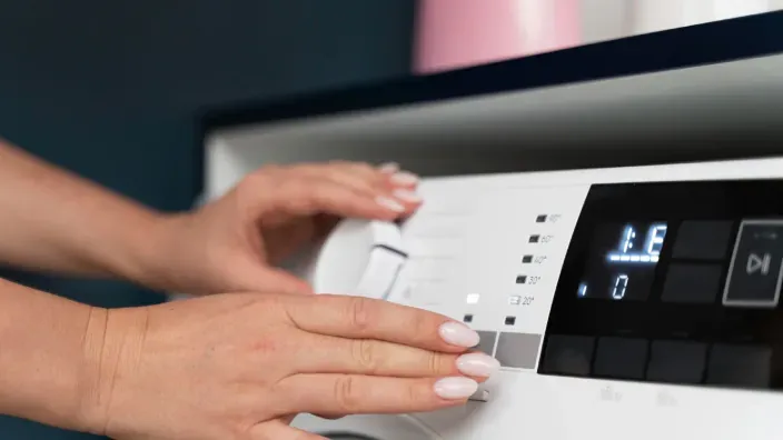 Manos ajustando el panel de control de una lavadora para seleccionar un programa de lavado eficiente.