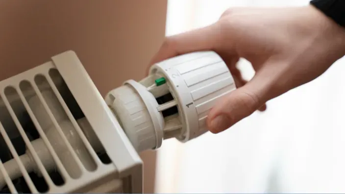 Mano ajustando la válvula termostática de un radiador para regular la calefacción del hogar