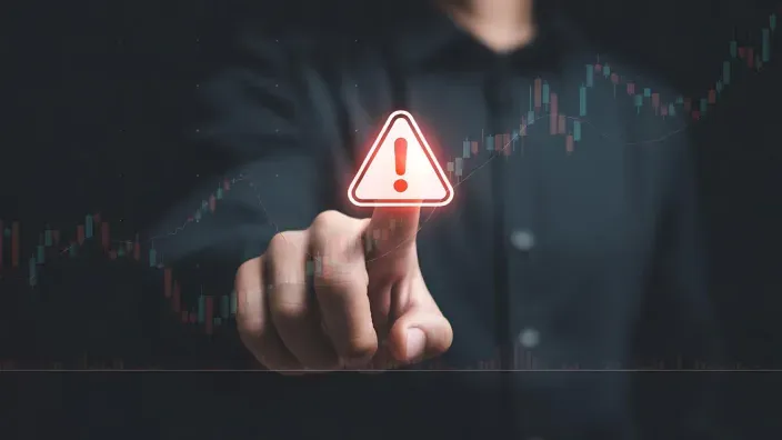 Alerta de riesgo financiero: dedo señalando un icono de advertencia sobre un gráfico de bolsa e inversión.