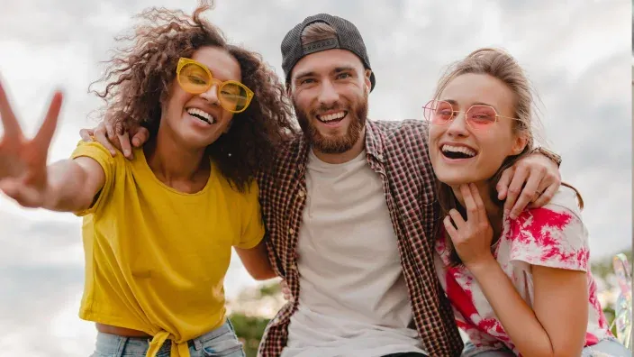 Tres jóvenes sonríen al aire libre posando juntos para una foto.