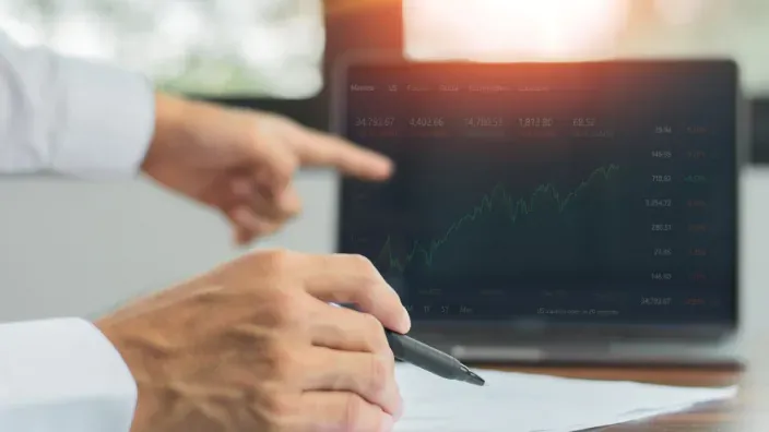 Manos señalando un gráfico de evolución bursátil en una pantalla durante un análisis de mercado