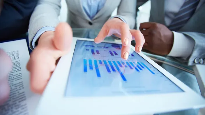 Profesionales analizando gráficos financieros en una tablet durante una reunión.
