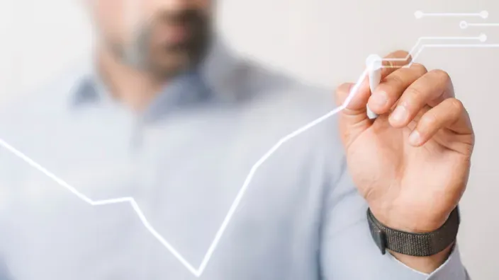 Hombre dibujando una gráfica ascendente en un panel de cristal para representar el crecimiento económico y financiero.