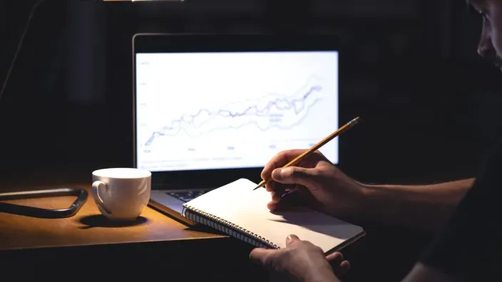 Persona analizando gráficos financieros en un portátil y tomando notas para planificar inversiones y ahorro