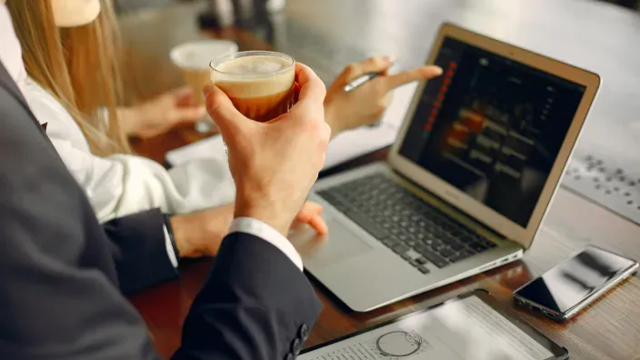 Personas analizando datos de inversión en un ordenador portátil durante una reunión con café.