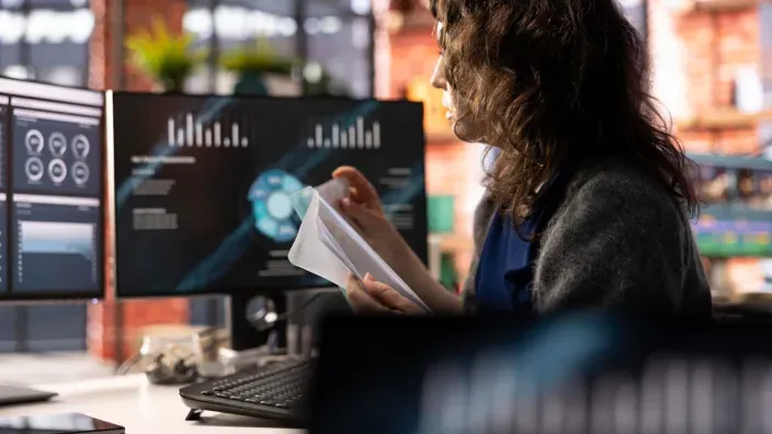 Mujer analizando gráficos en pantallas de oficina para la gestión de riesgos y análisis de datos en seguros.