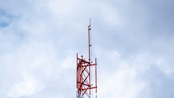 Antena de telecomunicaciones roja contra un cielo nublado. Infraestructura para la cobertura de la red de telefonía móvil.