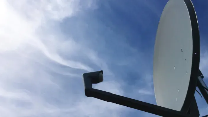 Antena parabólica orientada al cielo azul, representando la recepción de señal de televisión por satélite.