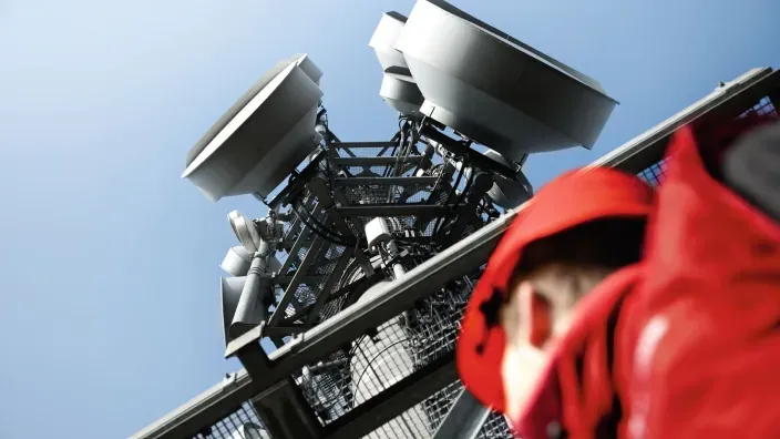 Antenas de telecomunicaciones en una torre con un casco rojo de Vodafone desenfocado en primer plano.
