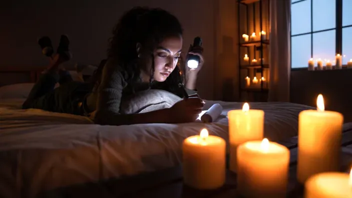 Mujer utilizando una linterna y velas en casa durante un apagón eléctrico nocturno.