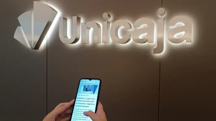 Usuario consultando la app móvil de Unicaja frente al logotipo iluminado del banco