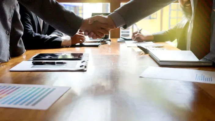 Apretón de manos profesional sobre una mesa con gráficos de inversión, simbolizando un acuerdo o alianza de negocios.