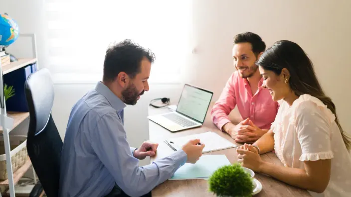 Pareja joven consultando con un asesor de seguros en una oficina para contratar una póliza.
