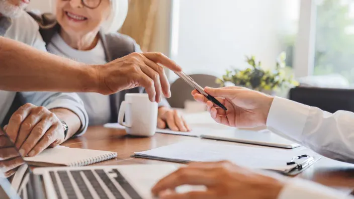 Pareja de personas mayores durante una reunión en una oficina, revisando documentos y opciones económicas