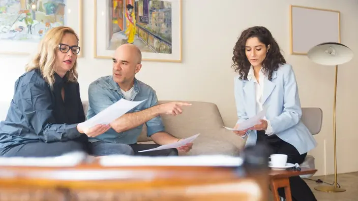Asesora profesional revisando documentos con una pareja de clientes en una sesión de consultoría privada.