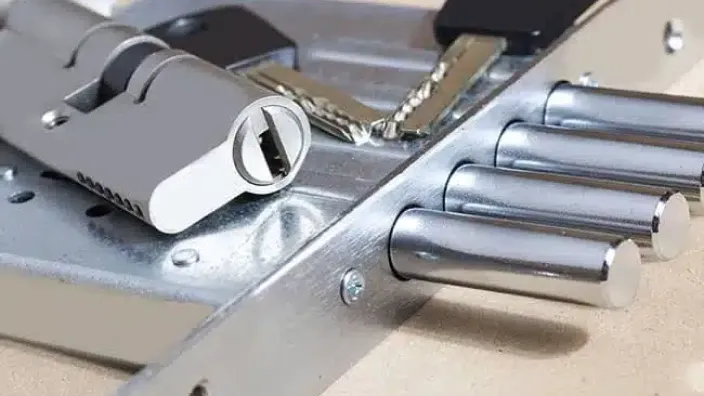 Primer plano del mecanismo de una cerradura de alta seguridad con bombín, llave y múltiples bulones o pestillos de acero.