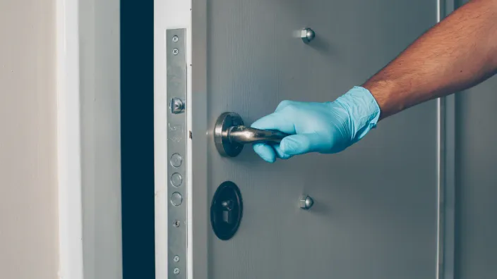 Mano con guante de látex azul abriendo puerta de seguridad de metal gris.