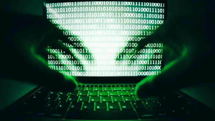 Silueta de un hacker frente a un portátil con código binario en pantalla representando un ciberataque.