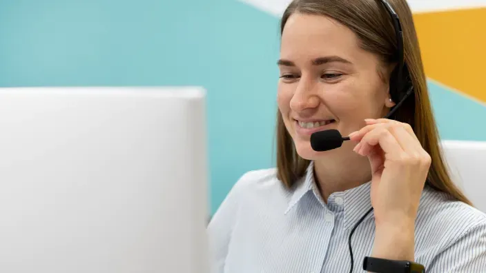 Agente de atención al cliente con auriculares sonriendo frente al ordenador.