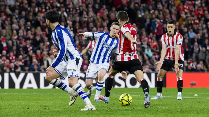 Jugadores del Athletic Club y la Real Sociedad disputan un balón durante un derbi vasco en San Mamés con el estadio lleno.