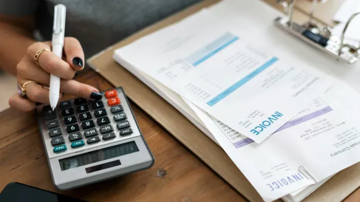 Mano de una mujer calculando los impuestos de varias facturas con una calculadora.