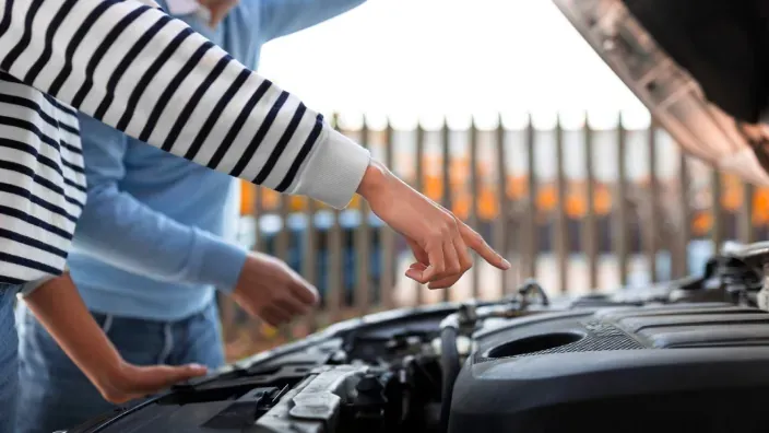 Pareja revisando el motor de un coche averiado con el capó abierto.