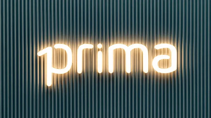 Logo retroiluminado de Prima Seguros, la compañía de seguros de coche online, sobre una pared de listones oscuros.