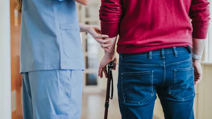 Enfermera asistiendo a paciente con bastón para caminar durante rehabilitación.