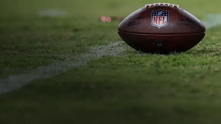 Balón de fútbol americano con el logotipo de la NFL apoyado sobre el césped del campo.