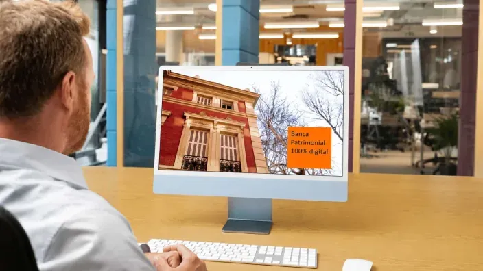Usuario consultando servicios de Banca Patrimonial 100% digital en su ordenador iMac desde la oficina.
