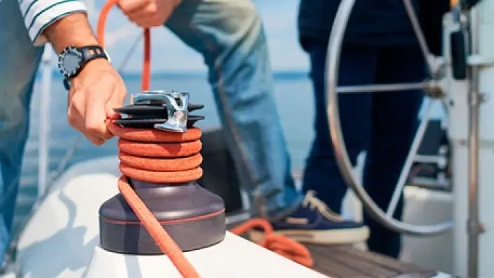Persona manejando cuerdas en un cabrestante de velero para representar la navegación y los seguros de barcos.