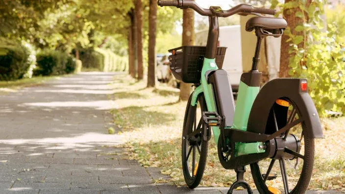 Bicicleta eléctrica urbana estacionada en un camino arbolado como alternativa de movilidad sostenible.