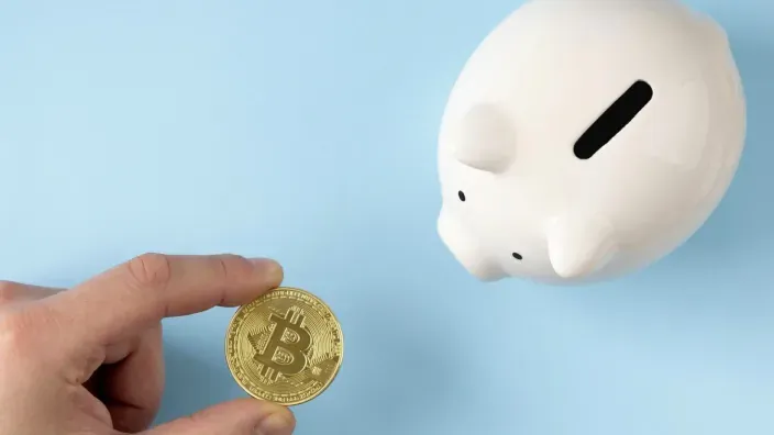 Concepto de ahorro e inversión en criptomonedas introduciendo moneda Bitcoin en una hucha.